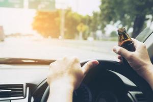 Mann hält Energy-Drink-Flasche beim Autofahren foto