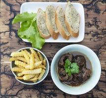 Rindfleischeintopf mit Pommes Frites und Knoblauchbrot servieren foto