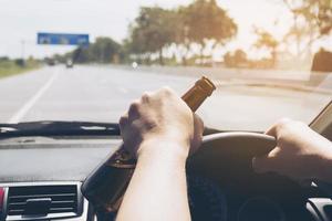 Mann hält Bierflasche beim Autofahren foto