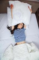 Mädchen schläft zu Hause in einem weißen Bett. junge frau, die zu hause in nachtwäsche auf der weißen bettwäsche im bett schläft, draufsicht. foto