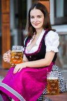 sexy russische frau im bayerischen kleid, das bierkrüge hält. foto