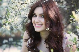 Schönes weißes europäisches Mädchen mit sauberer Haut im Park mit blühenden Bäumen foto