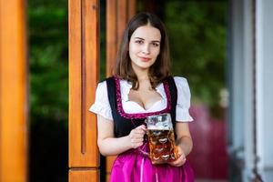 sexy russische frau im bayerischen kleid, das bierkrüge hält. foto