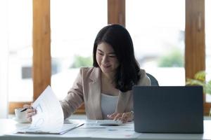 asiatische geschäftsfrau, die einen taschenrechner und einen laptop verwendet, um mathematische finanzen auf einem hölzernen schreibtisch, steuer, buchhaltung, statistikbericht und analytisches forschungskonzept zu machen. foto