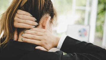 junge asiatin sitzt bei der arbeit und hat nackenschmerzen foto