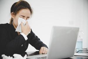 Kranke junge asiatische Geschäftsfrau, die allein bei der Arbeit sitzt, niest foto