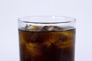 Ein isoliertes Glas schwarzer Cola mit Eis wird auf weißem Hintergrund gefüllt foto