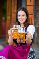 sexy russische frau im bayerischen kleid, das bierkrüge hält. foto