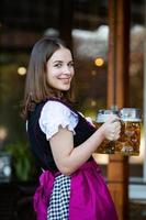 sexy russische frau im bayerischen kleid, das bierkrüge hält. foto