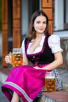 sexy russische frau im bayerischen kleid, das bierkrüge hält. foto