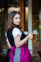 sexy russische frau im bayerischen kleid, das bierkrüge hält. foto