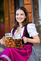 sexy russische frau im bayerischen kleid, das bierkrüge hält. foto