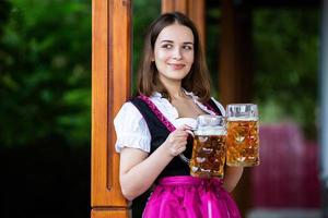 sexy russische frau im bayerischen kleid, das bierkrüge hält. foto