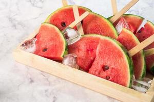 Wassermelonenscheiben auf Stöcken mit Eiswürfeln. frisches wassermeloneneis am stiel in holzschale. foto