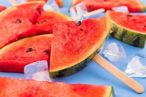 Wassermelonenscheiben auf Stöcken mit Eiswürfeln. frisches wassermeloneneis am stiel auf blauem hintergrund. foto