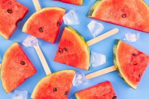 Wassermelonenscheiben auf Stöcken mit Eiswürfeln. frisches wassermeloneneis am stiel auf blauem hintergrund. foto