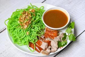 Jade-Nudeln asiatisches thailändisches Essen, gebratene Ente mit Jade-Nudeln auf weißem Teller und Entensauce, grüne Nudeln chinesisches Essen foto
