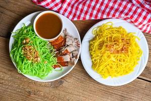 Jade-Nudeln und gelbe Nudeln asiatisches Thailand-Essen, gebratene Ente mit Jade-Nudeln auf weißem Teller und Holzhintergrund mit Entensoße, chinesisches Essen mit grünen Nudeln foto