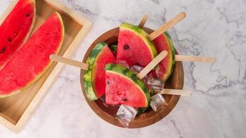 Wassermelonenscheiben auf Stöcken mit Eiswürfeln. frisches wassermeloneneis am stiel in holzschale. foto