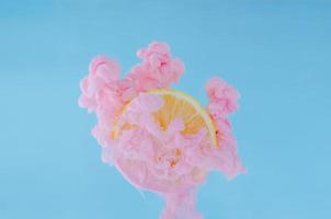 Zitronenscheibe mit teilweisem Fokus auf das Auflösen der rosa Plakatfarbe in Wasser foto