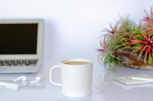 eine tasse kaffee auf dem bürotisch mit luftpflanze tillandsia und modernen büromaterial. foto