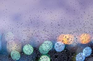 Regentropfen auf Glasfenster in der Monsunzeit mit buntem Bokeh-Licht vom Hintergrund der Stadtgebäude. foto