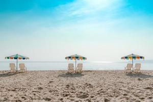 weißer Liegestuhl und Sonnenschirm am tropischen Strand mit blauem Himmel foto