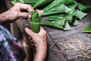 alte großmutterhände, die mit bananenblatt arbeiten, um blumenbehälter herzustellen - leute, die traditionelle gegenstände für die teilnahme an lokalen zeremonien herstellen foto