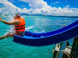 asiatischer mann, der in der urlaubszeit den schieberegler auf dem boot mit einem erstaunlichen idyllischen ozean und blau spielt foto