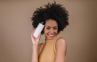 lateinische frau der schönheit mit afrofrisur. brasilianische Frau. leere shampooverpackung halten. Lockige haare. Frisur. Pastellhintergrund. foto