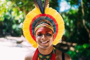 indianer aus dem pataxo-stamm mit federkopfschmuck, der in die kamera schaut. indigener mann aus brasilien, mit traditionellen gesichtsbemalungen