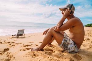 Nahaufnahme Porträt eines lateinamerikanischen Mannes, der auf dem Sand sitzt und Musik hört foto