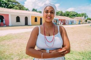 Fröhliche Brasilianerin in traditioneller bahianischer Tracht, verschränkte Arme im historischen Zentrum von Porto Seguro im Hintergrund foto