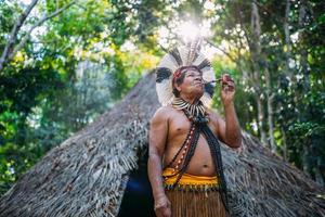 Schamane des Pataxo-Stammes, trägt Federschmuck und raucht eine Pfeife. brasilianischer Indianer, der nach rechts schaut foto