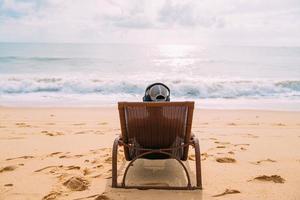 sommerferien, technologie- und internetkonzept. lateinamerikanischer mann sitzt auf dem strandkorb, hört musik mit kopfhörer und sonnt sich am strand foto