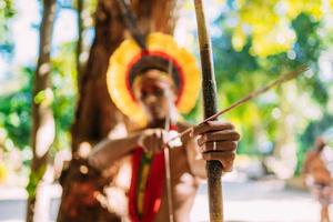 Indianer vom Pataxo-Stamm mit Pfeil und Bogen. brasilianischer Indianer mit Federschmuck und Halskette. Fokus auf Pfeil und Bogen foto