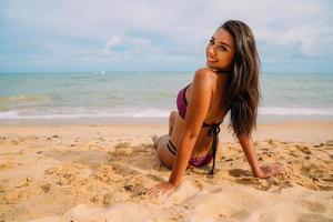 Silhouette einer jungen Frau am Strand. lateinamerikanische Frau, die an einem schönen Sommertag auf dem Strandsand sitzt und in die Kamera schaut foto