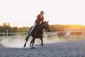 junge jockette in einem helm, der auf dem pferd auf der koppel reitet. foto