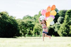 junges Mädchen, das mit Luftballons auf der Wiese läuft. foto