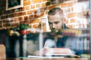 Mann in den Dreißigern sitzt am Tisch und schreibt foto