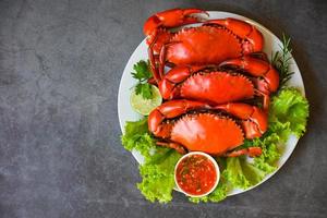 frische Krabben auf weißem Teller und Meeresfrüchtesoße, Krabbenkochen im Restaurant gekochte oder gedünstete Krabben rot, Meeresfrüchteteller mit Kräutern, Gewürzen, Rosmarin, Zitrone, Limette, Salat, Gemüse foto