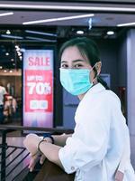 asiatische frauen, die masken tragen, gehen in den einkaufszentren einkaufen, haben vor dem geschäft ein rabattschild aufgestellt, um kunden anzulocken. Auch wenn das Zeichen verschwommen ist, wissen wir, dass es 70 Prozent günstiger ist. foto