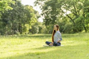 junge asiatische frau, die meditation im park praktiziert. durch Glück aus innerem Frieden. foto