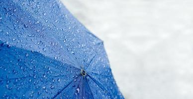breite leinwand aus regentropfen auf blauem regenschirm mit verschwommener straße an regnerischen tag. foto