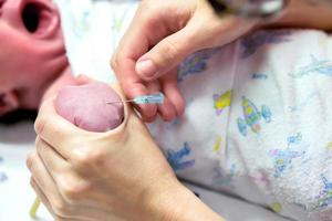 Nahaufnahme von Krankenschwesterhänden, die die Handgelenke des kranken Babys stechen, um die Kochsalzlösung für das schwerkranke Neugeborene vorzubereiten. foto