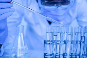 Biochemiker führen Experimente durch, um neue Medikamente zu entdecken. Forscher arbeiten in Wissenschaftslabors. ein männlicher wissenschaftler, der eine schutzbrille und gartenhandschuhe trägt, tropft chemikalien, um einen impfstoff zu testen. foto