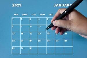 kalender januar 2023 mit hand, die schwarzen stift auf blauem hintergrund hält. foto