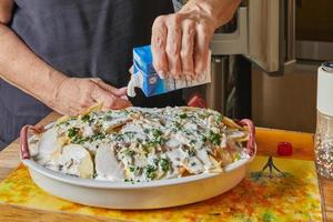 koch streicht creme fraiche auf ein fischgratin mit kartoffeln und äpfeln. exquisite französische Küche foto