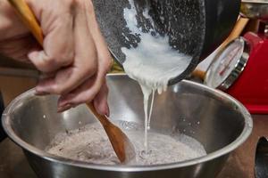 Küchenchef gießt Schlagsahne in eine Schokoladenkuchenmischung mit Birnen und Nüssen. Schritt für Schritt Rezept foto