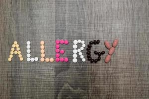 das Wort Allergie geschrieben mit Pillen auf einem hölzernen Hintergrund. foto
